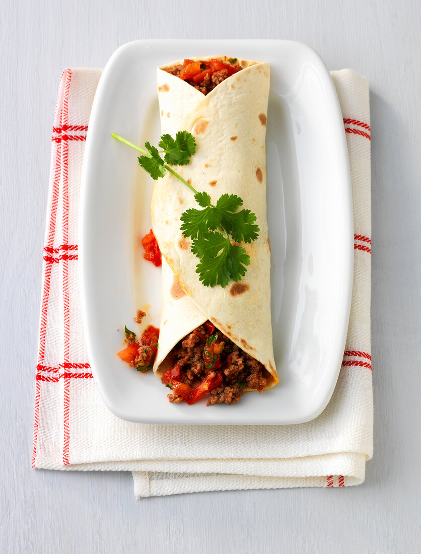 Plate of minced meat wrapped in tortilla on folded napkin