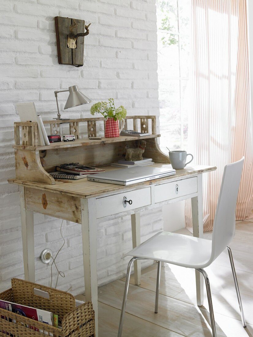 A white, shabby style wooden bureau with a modern chair and a newspaper holder