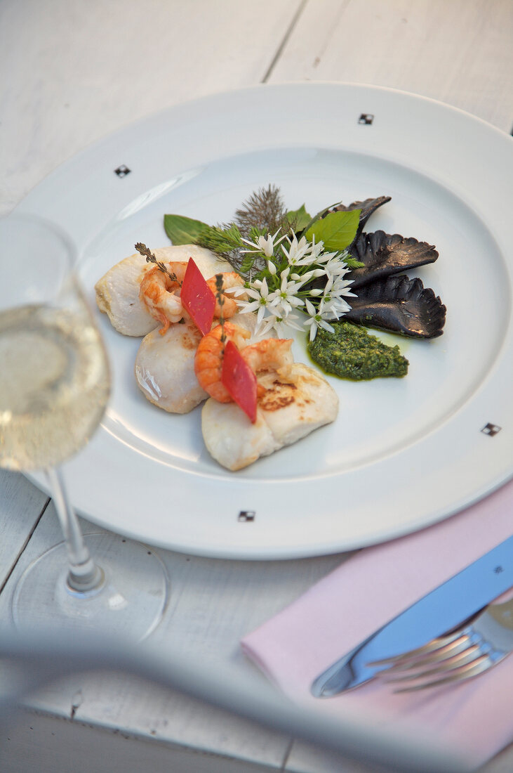 Zander cheeks with crayfish, black ravioli, pesto and herbs on plate