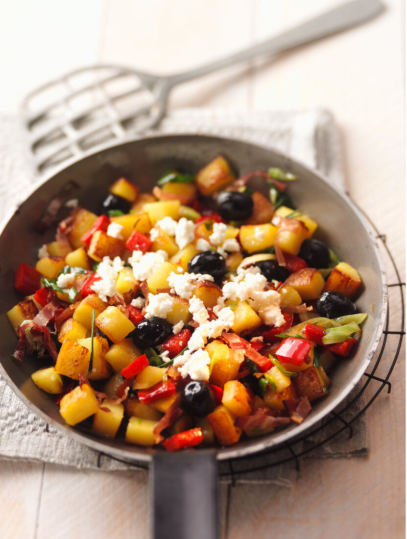 Potato cubes with olives and red peppers in pan