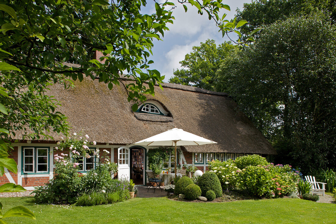 Exterior of thatched cottage with garden and terrace in the sunshine