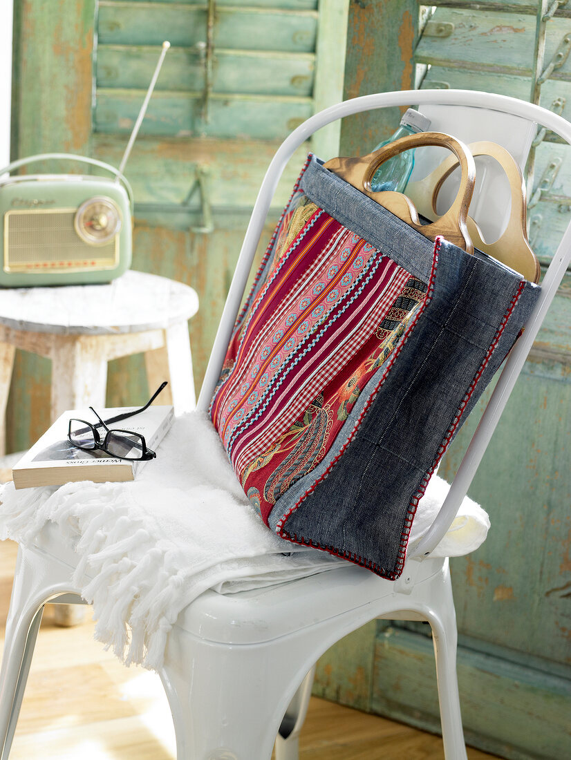 Large tote denim bag decorated with braids and ribbons on white chair