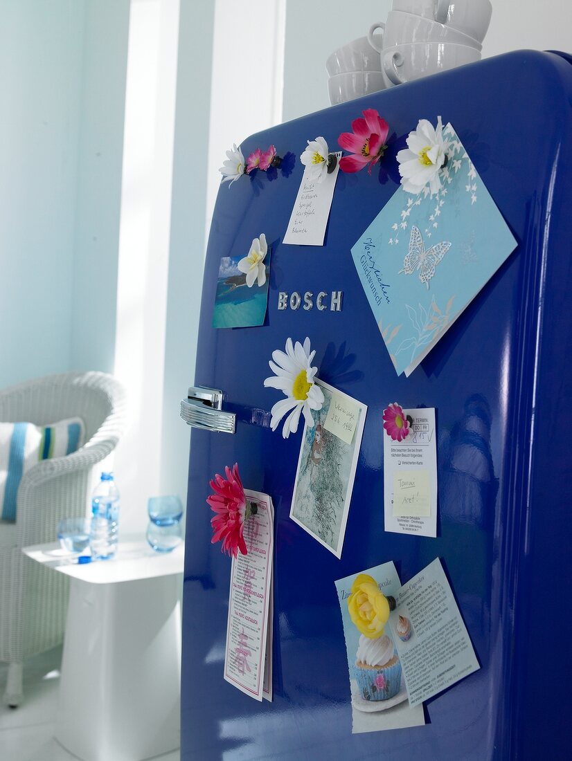 Close-up of blue fridge door with magnet fabric flowers and labels