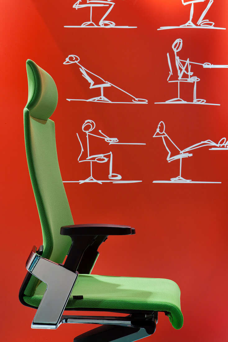 Close-up of green office chair in front of ergonomic graffiti on orange wall