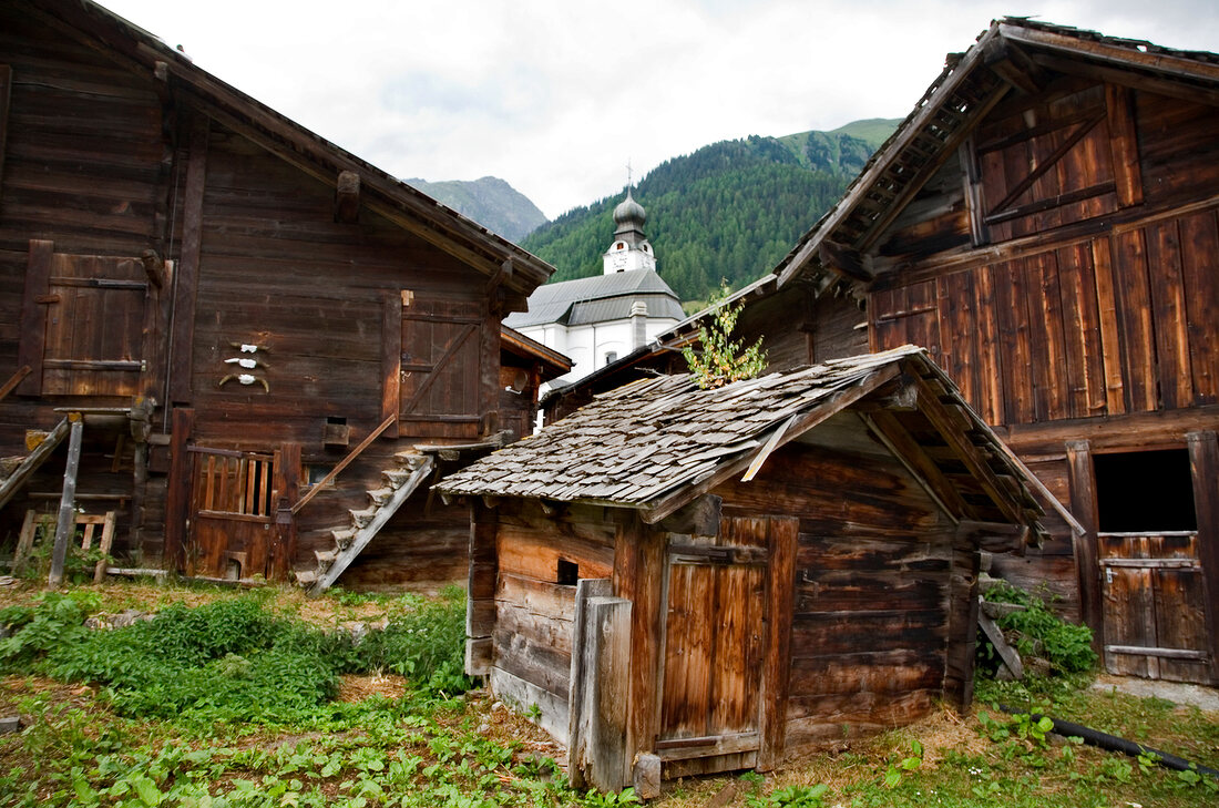 Wallis, Holzhäuser und Scheunen in Goms, Barockkirche im Hintergrund