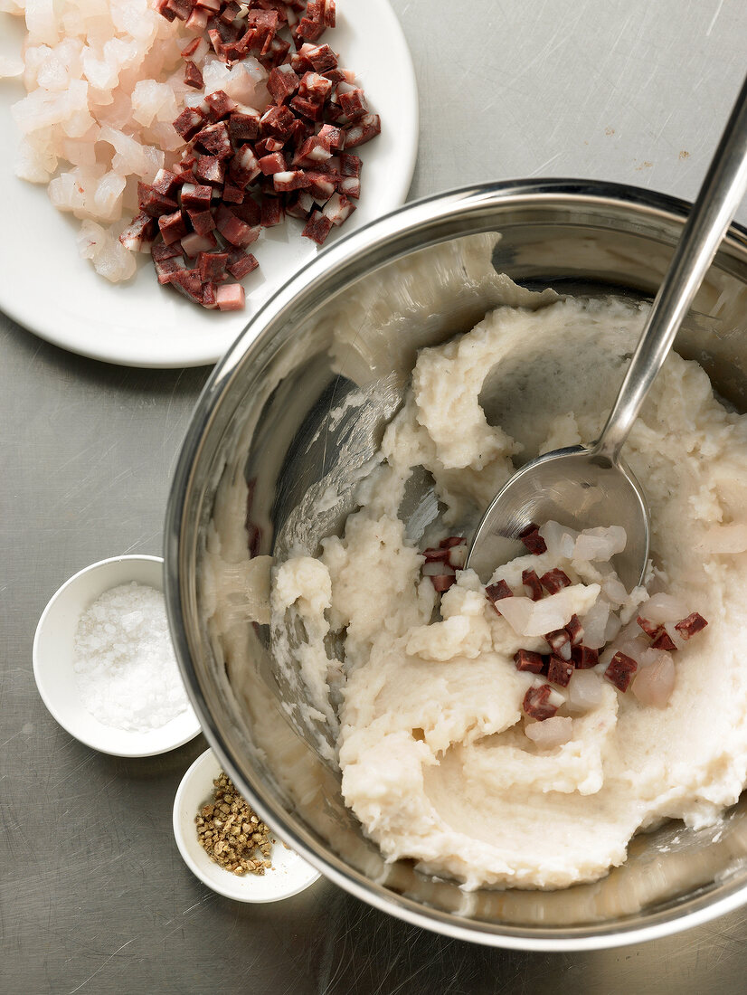 Folding fish stuffing with pieces of zander in bowl with spoon