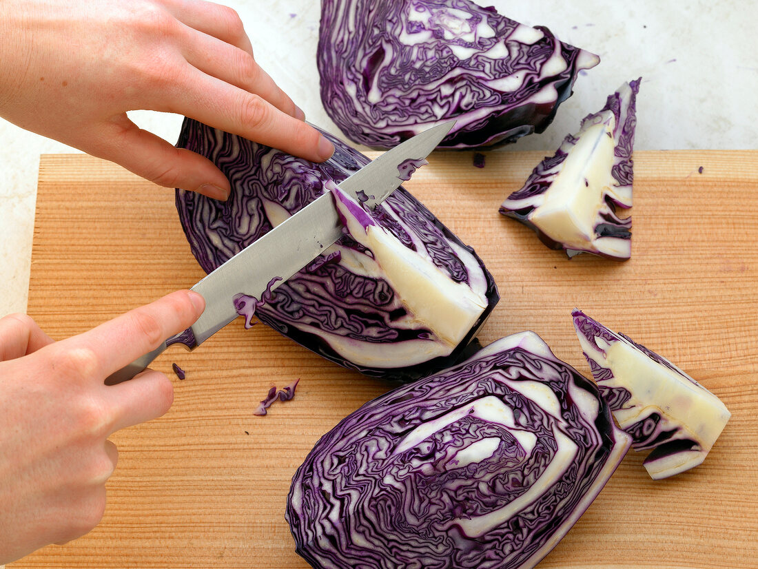 Cutting red cabbage quarters with knife on cutting board, step 1