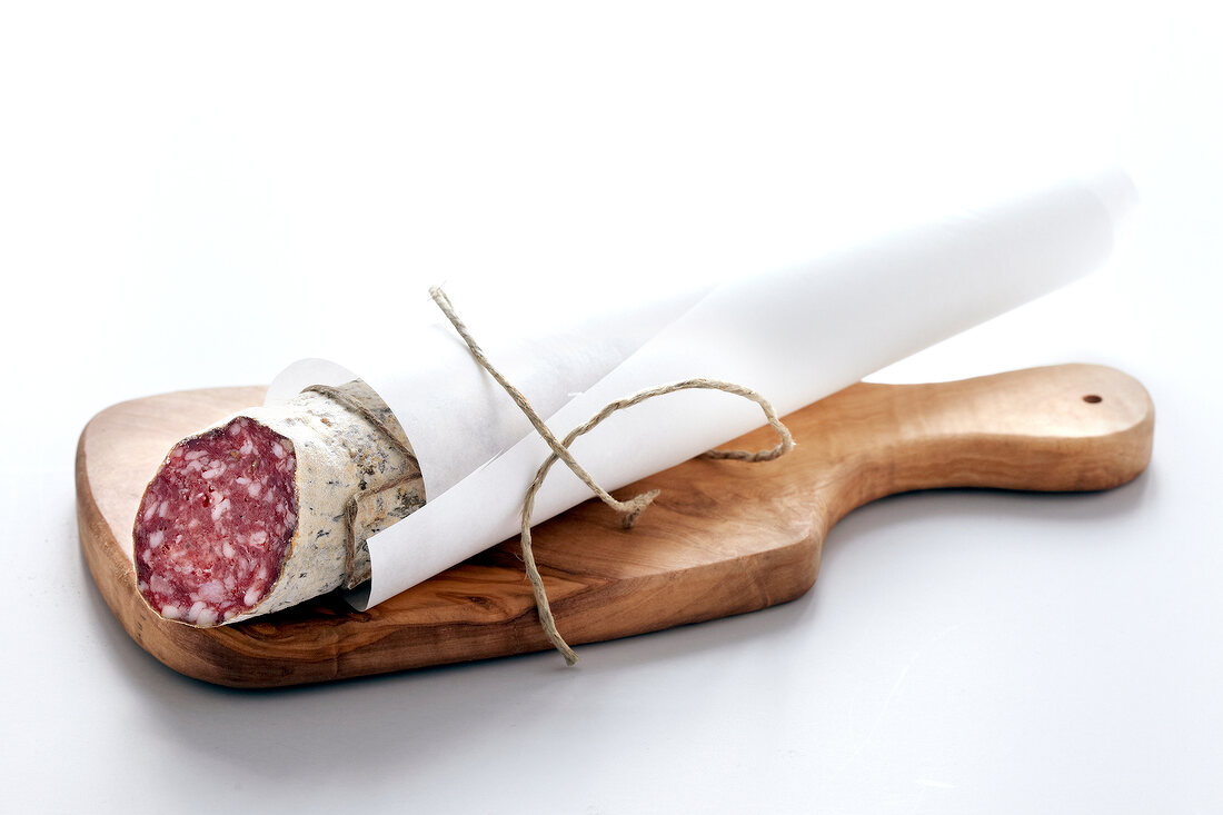 Salami am Stück, in Papier gewickelt auf Holzbrett