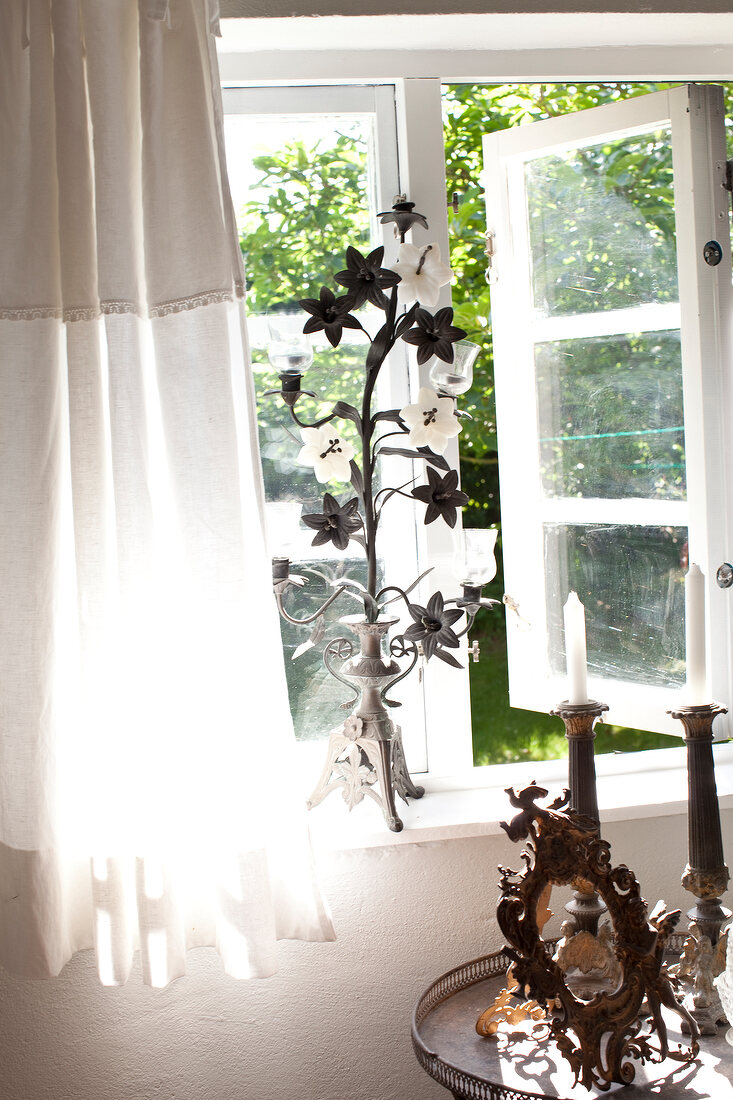 Antique candlesticks in front of window with metal flower decoration on window sill