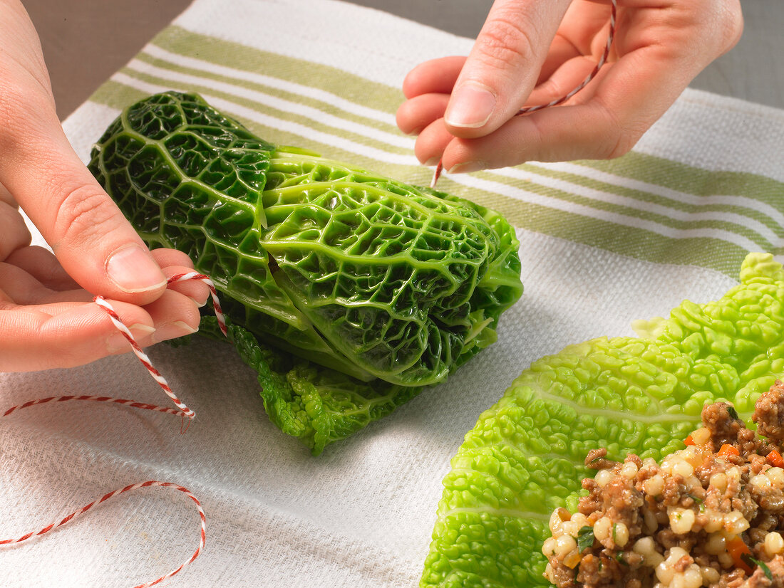 Close-up of hands tying cabbage rolls with kitchen string, step 1