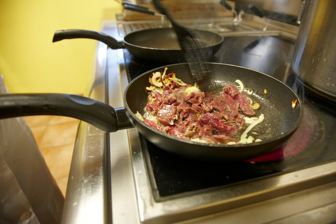 Sliced venison meat being fried in pan