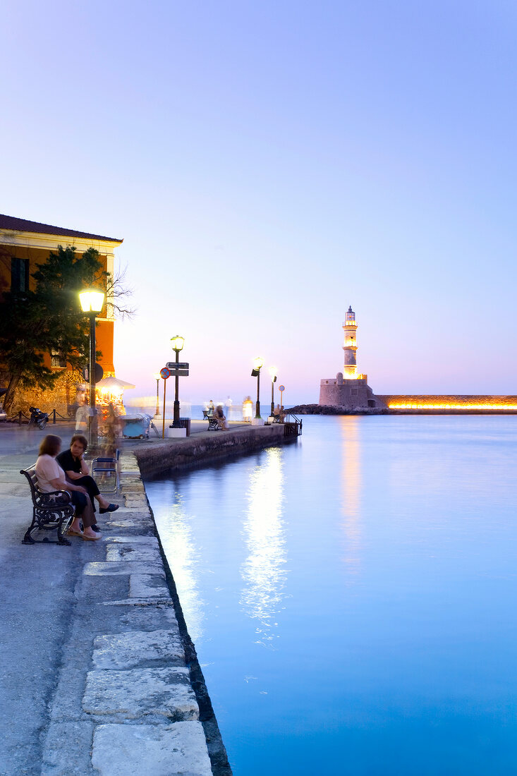 Chania Lighthouse at dawn and people sitting on bench at promenade near sea, Crete, Greek