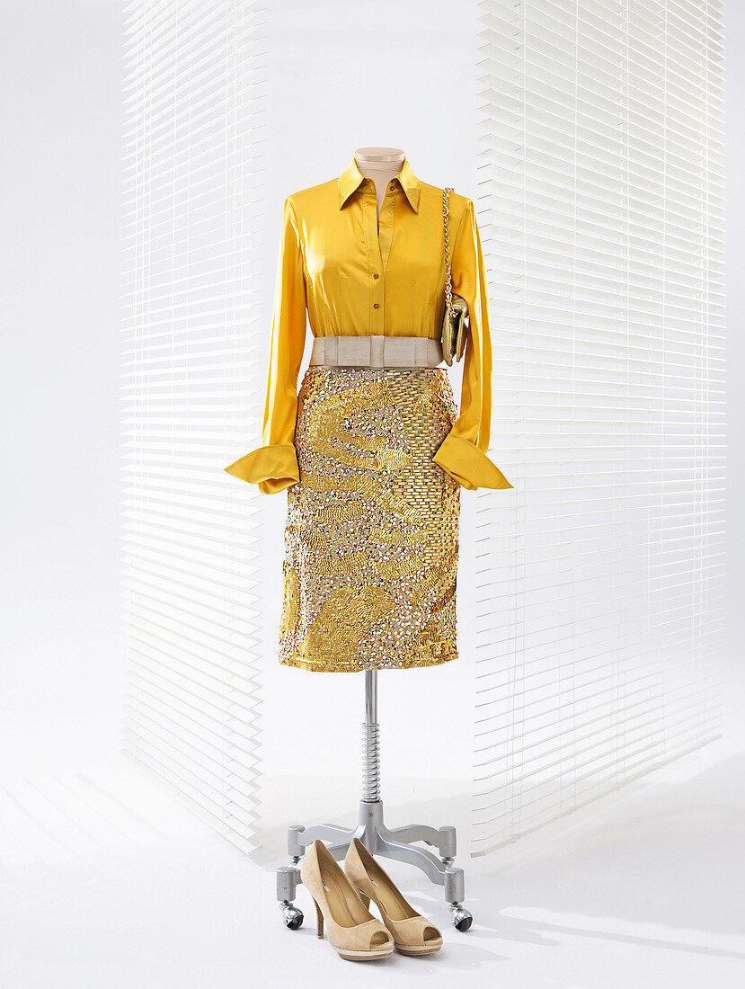 Yellow silk blouse and pencil skirt studded with sequins on clothes stand