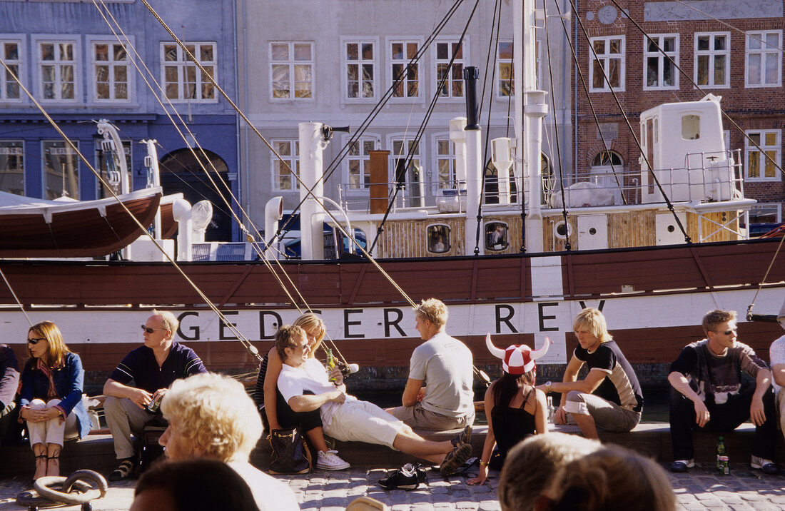People relaxing in front of ship at Nyhavn harbour, Copenhagen, Denmark