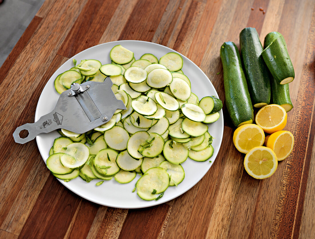 Slices of zucchini with truffle slicer on plate, half lemon and zucchini on wood