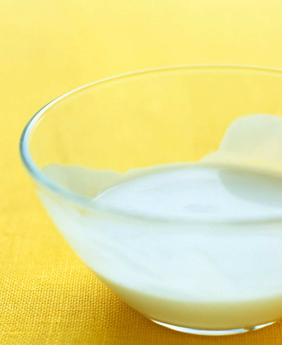 Close-up of coconut milk in glass bowl on yellow background