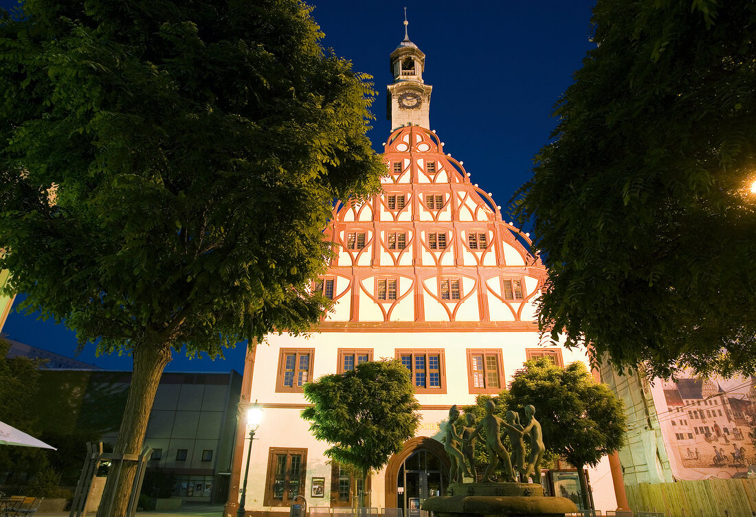 View of illuminated Zwickau Gewandhaus with trees at dusk, Saxony, Germany