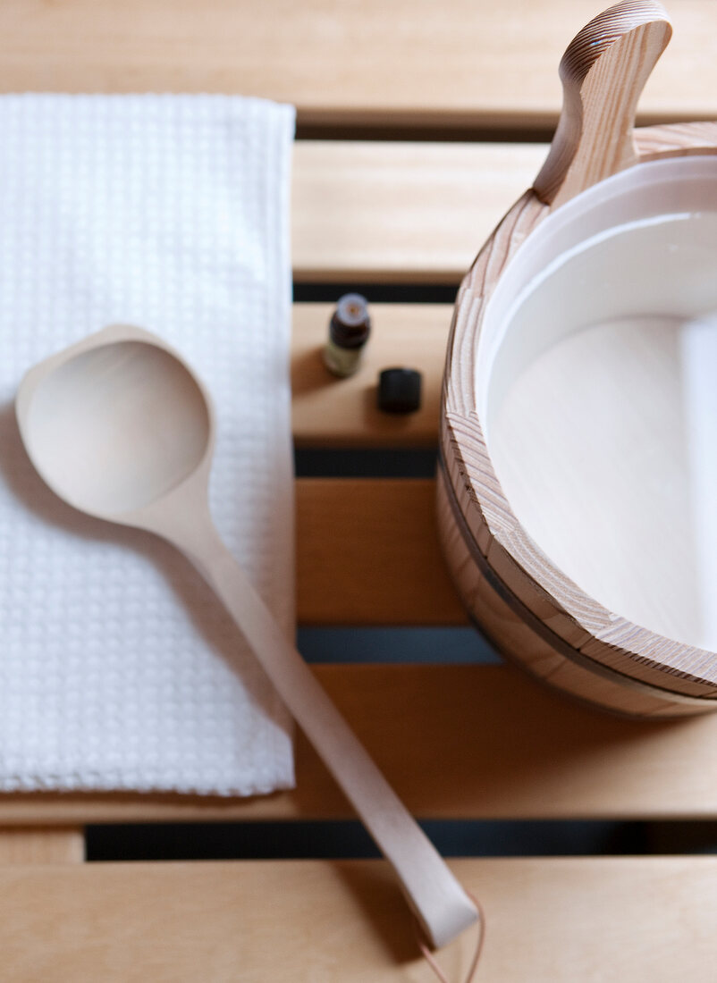 Wooden container with essential oil and wooden spoon on tissue, overhead view