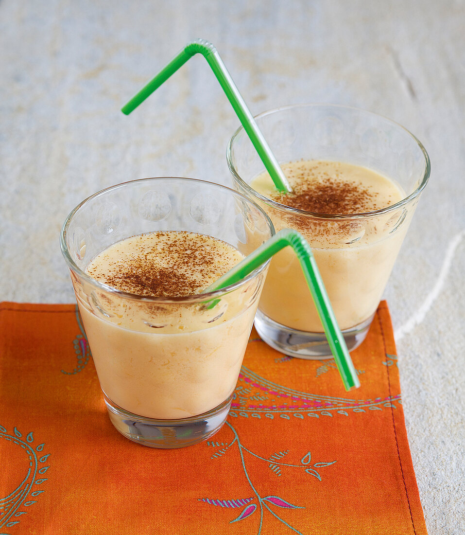 Two glass of mango lassi and tangerine with straws