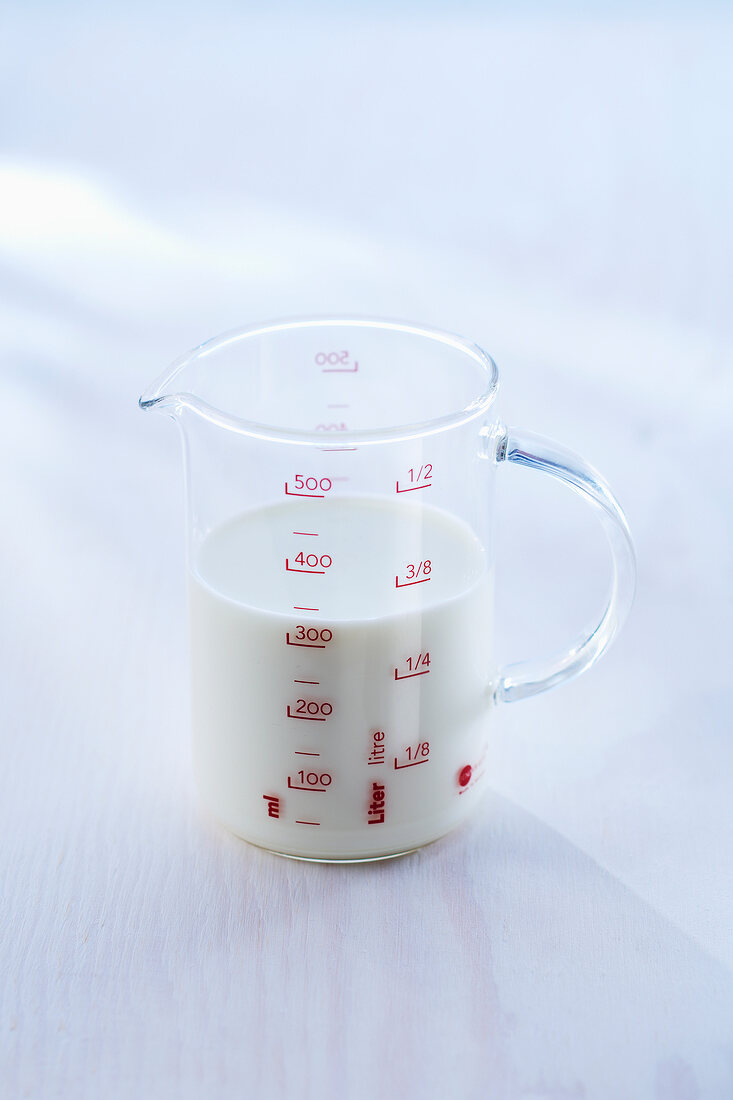 Measuring cup with cream on white background