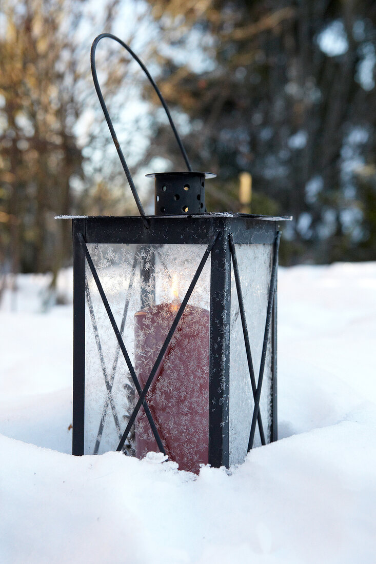 Tin lantern with red candle in snow