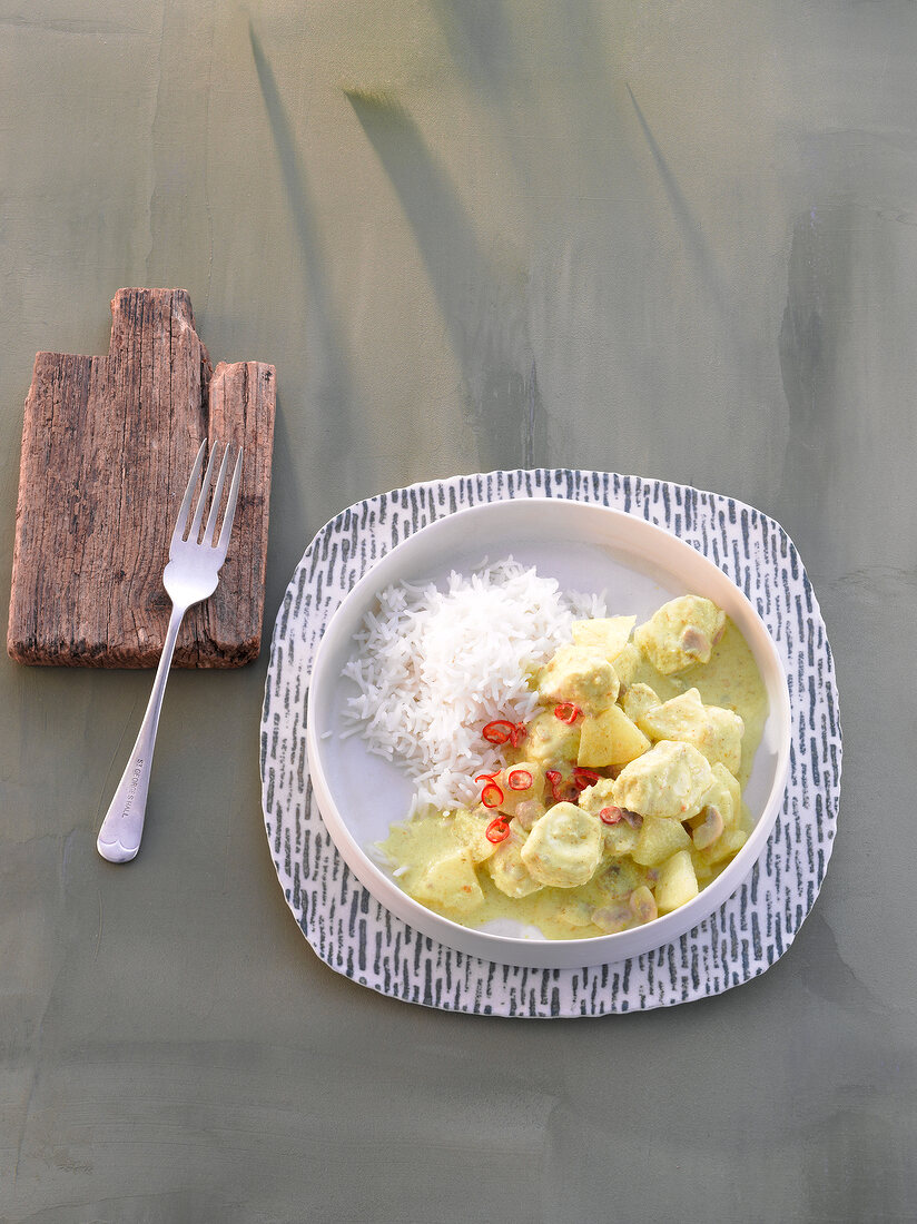 Fish curry with rice on plate and fork on wooden table coaster