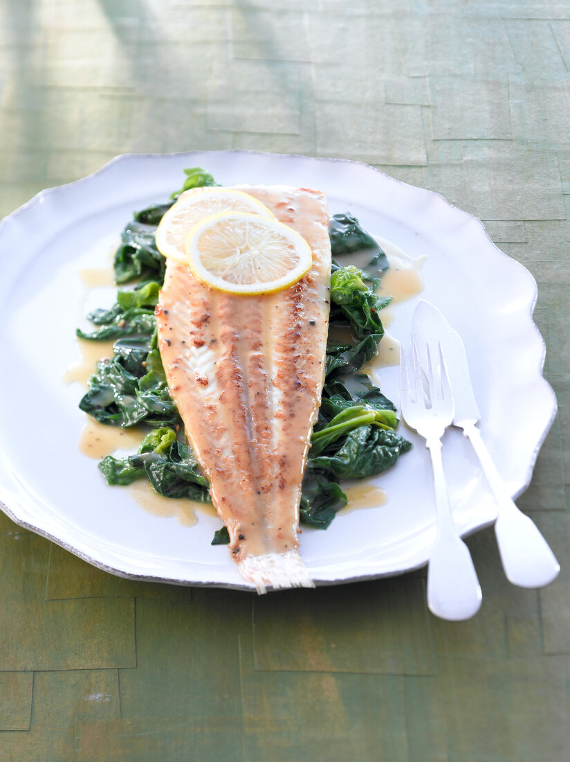 Fried sole with spinach and lemon wedges on plate