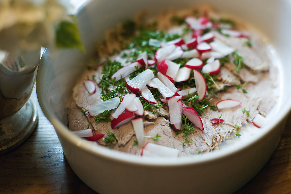 Close-up of veal garnished with radish and herbs in bowl