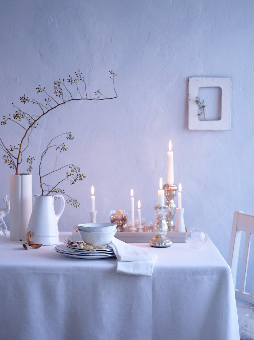 Tisch, Kerzenleuchter, gestapeltes Geschirr, Vasen mit Zweigen