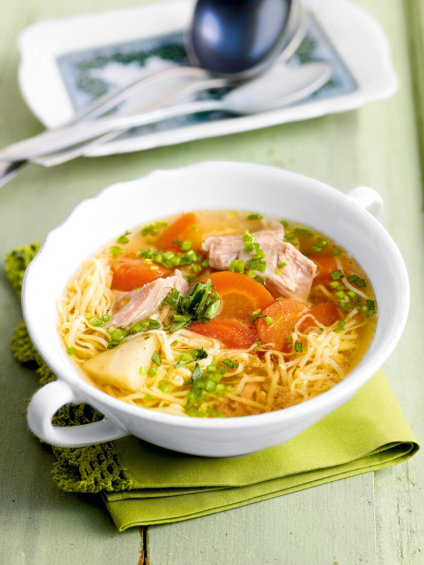 Chicken broth with lovage and egg noodles in serving bowl on folded napkin