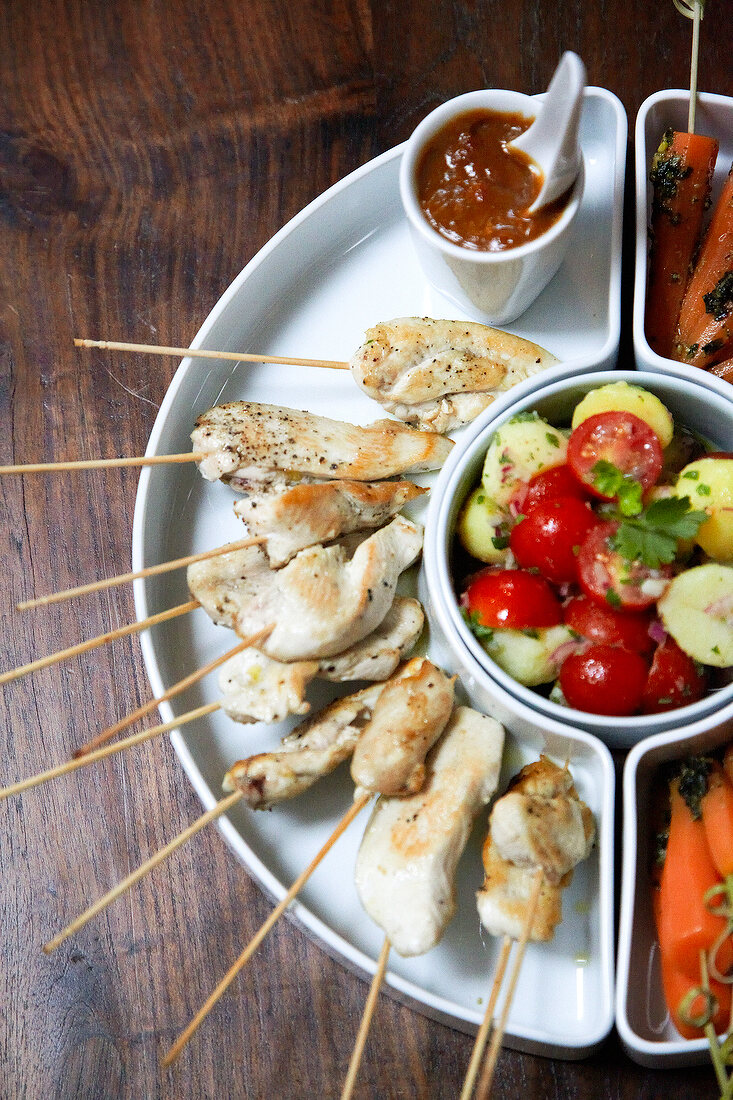 Chicken teriyaki in semi circle dish with peanut and chilli sauce in bowl