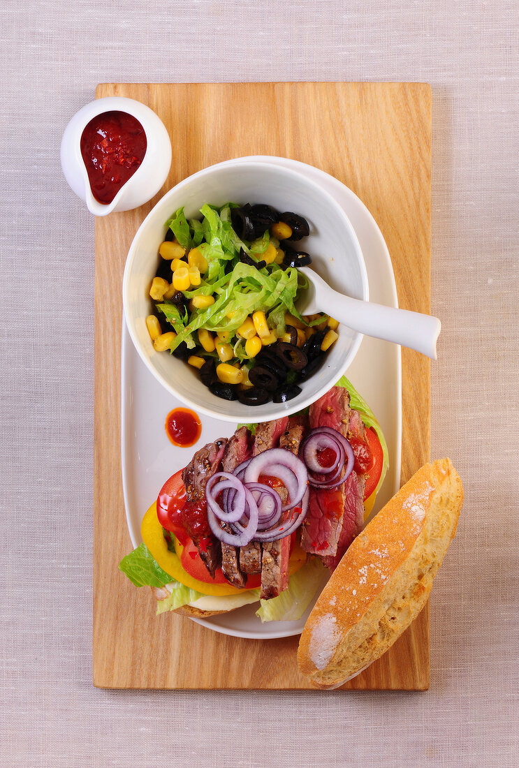 Steak burger in serving dish with corn salad and dip in bowl