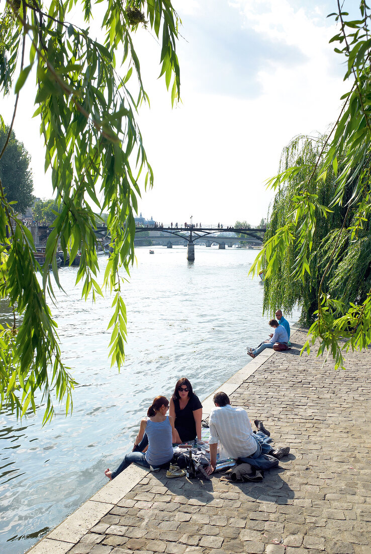 People sitting on dock beside Seine river, Paris, France