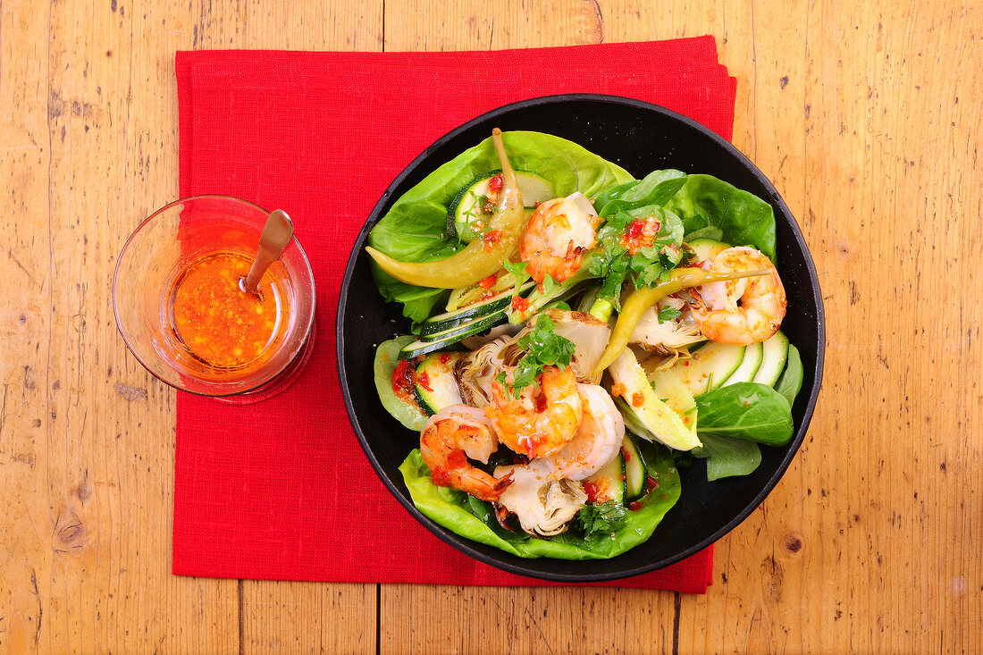 Mixture of lettuce with zucchini, artichokes and shrimps on plate