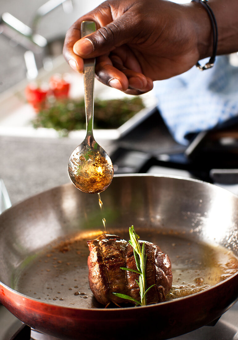 Close-up of man's hand adding oil to fillets in skillet