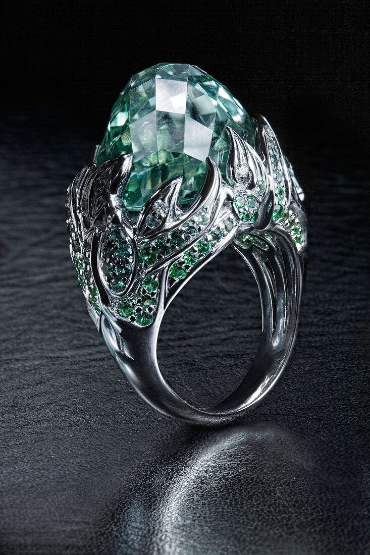 Close-up of white gold ring with green amethyst and sapphires on grey background