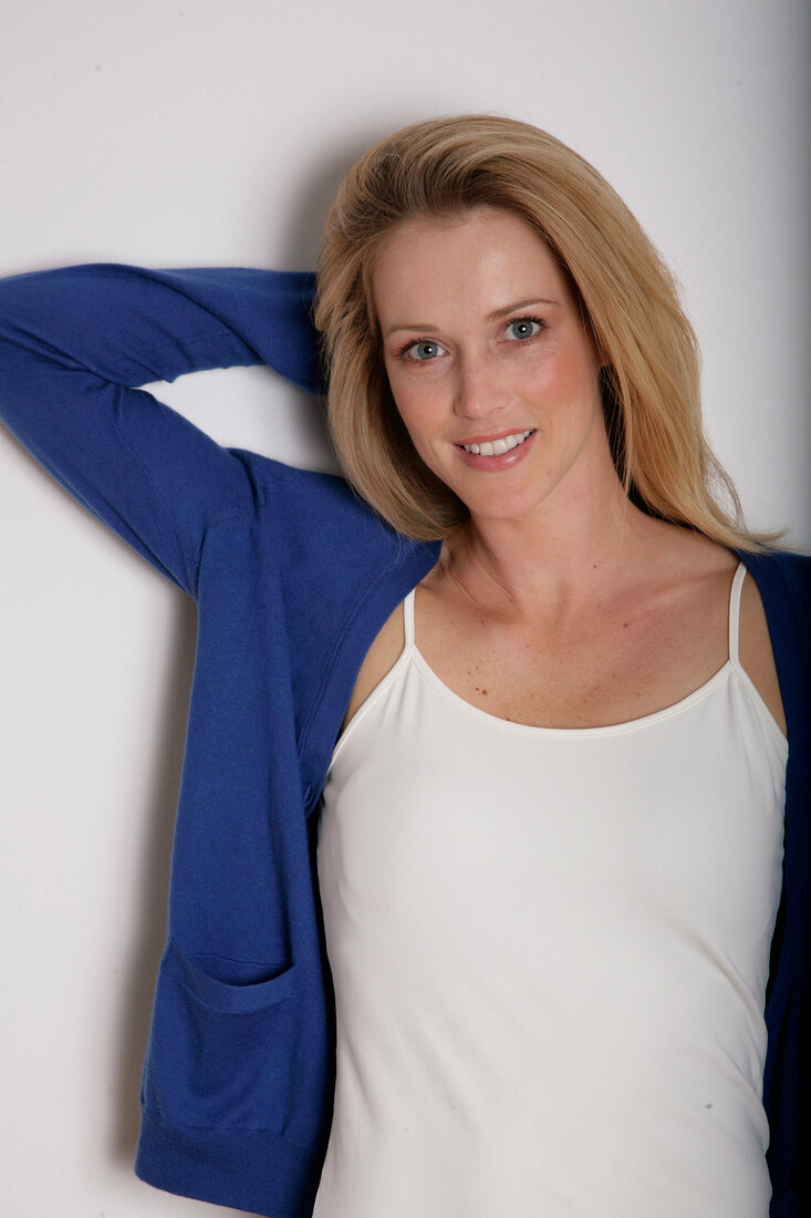Beautiful blonde woman wearing blue sweater over white spaghetti with hand behind head