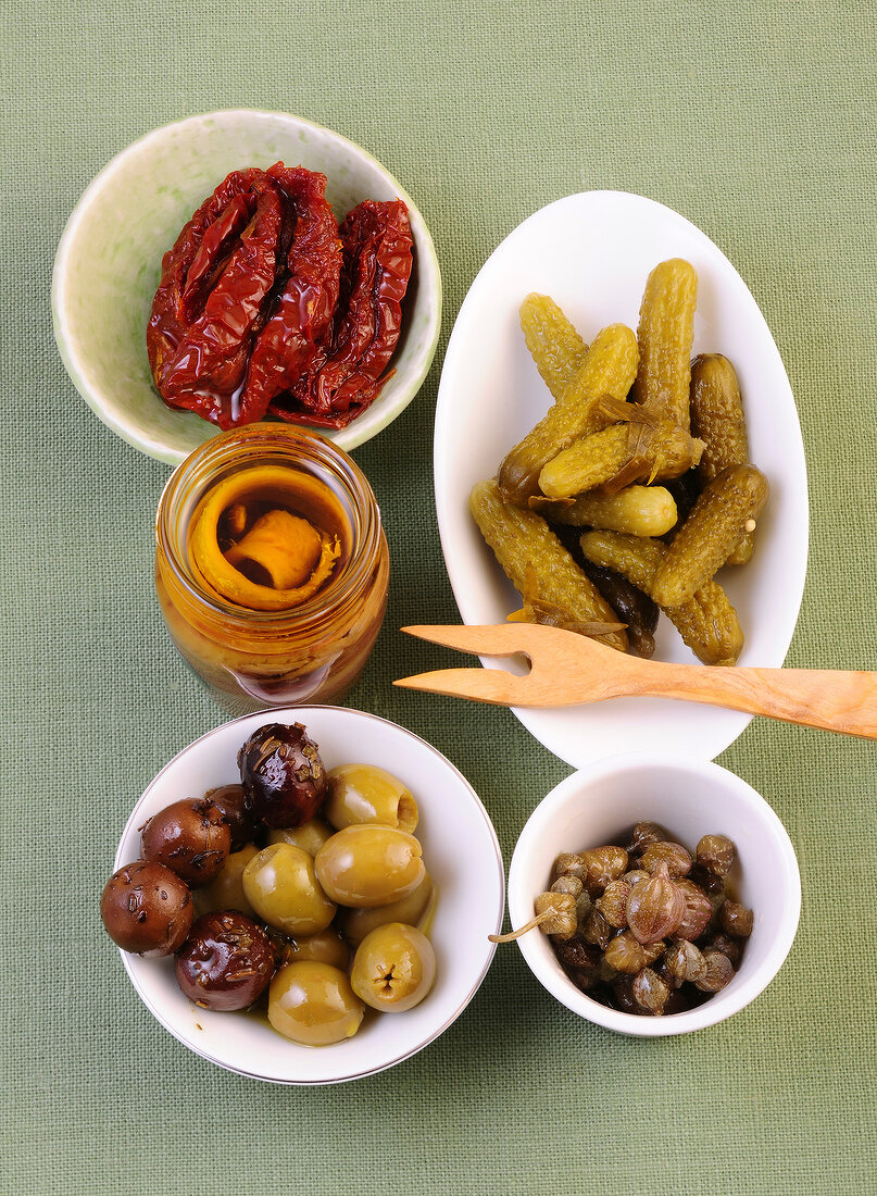 Olives, capers, cucumbers, tomatoes, anchovies in bowls and jar