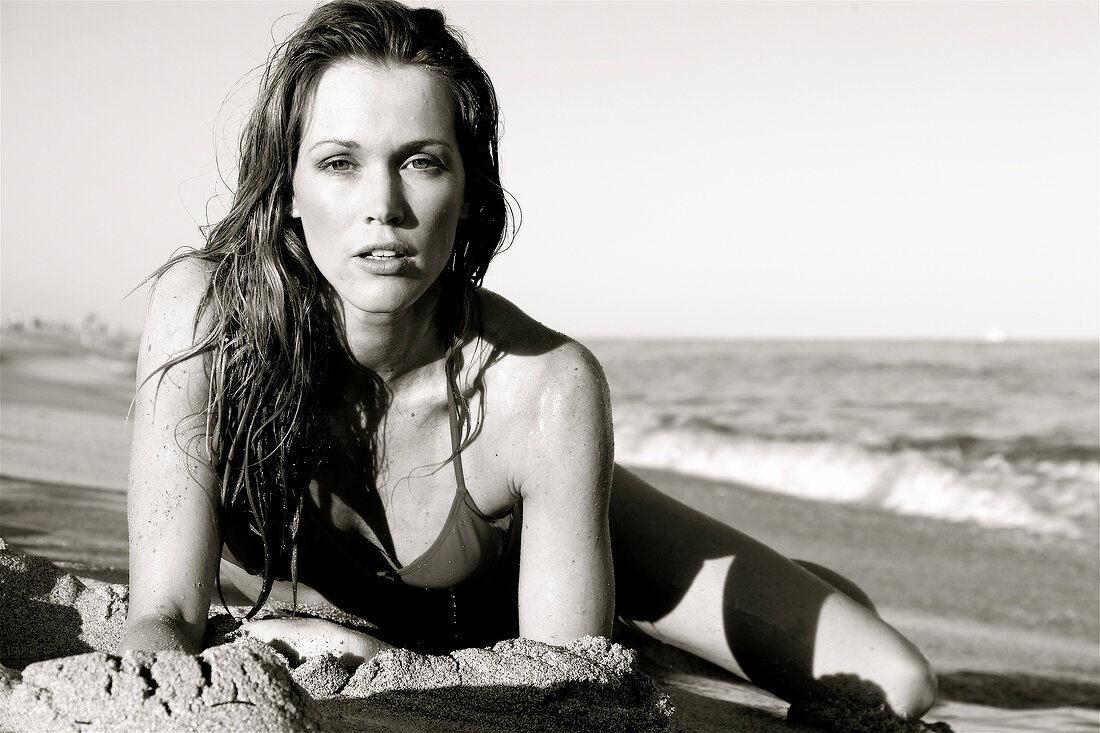 Portrait of blonde woman wearing bikini lying on her front on sand, black and white