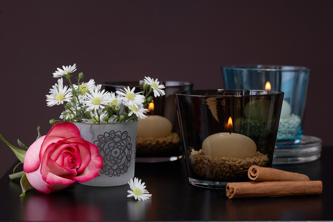 Lanterns with lit candles, cinnamon stick and daisies in flower vase as decoration