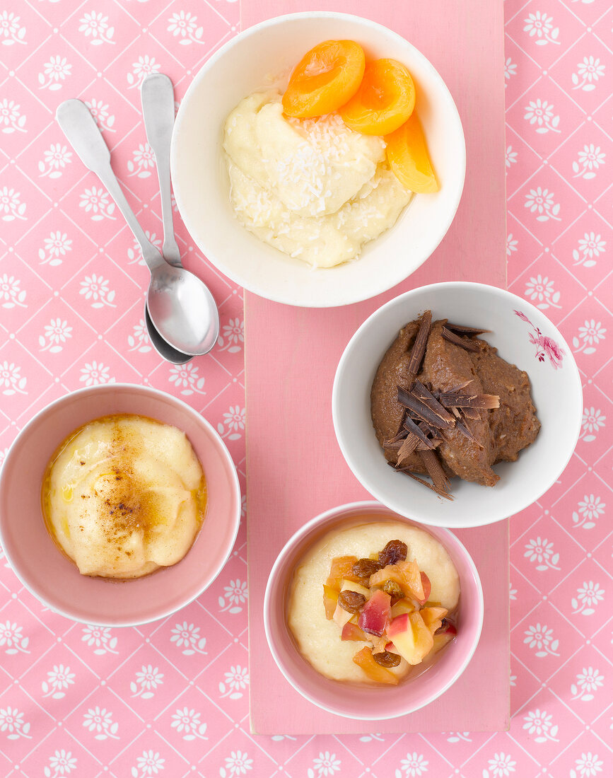 Four varieties of semolina in bowls on pink background, overhead view