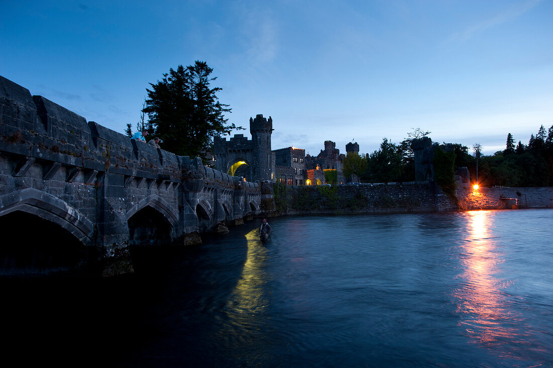 Illuminated Ashford Castle and Bridge over Cong canal at dusk, Ireland, UK