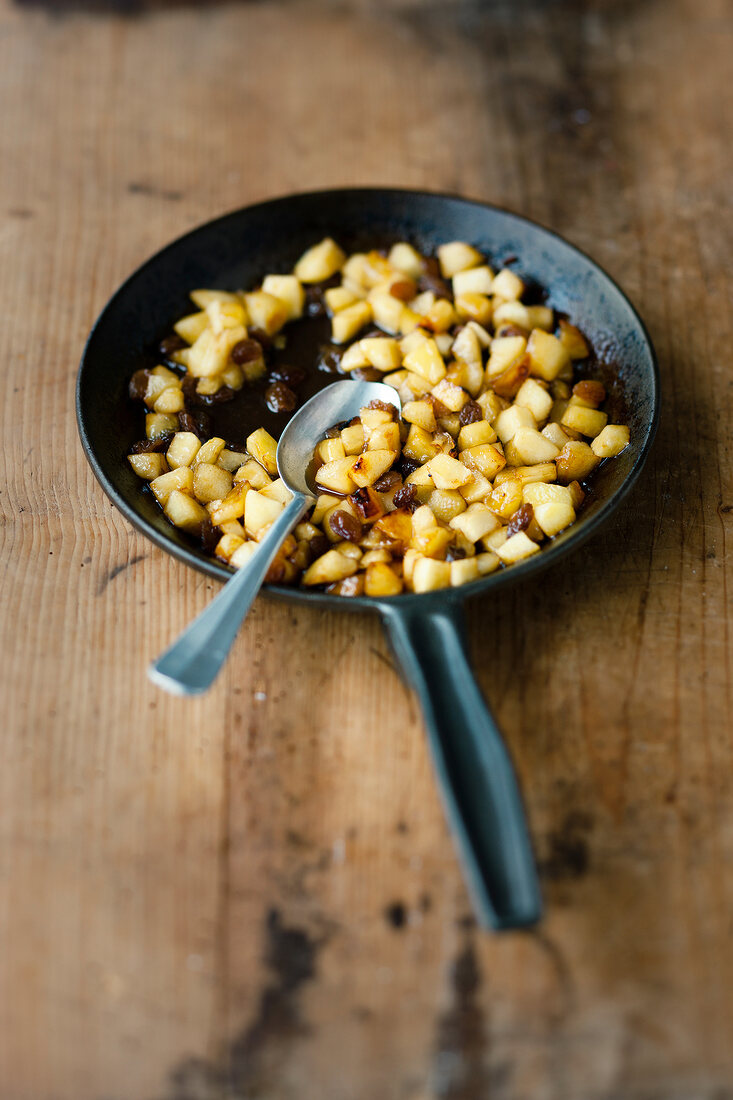 Chopped apple cubes mixed in caramel with spoon in pan on wooden surface