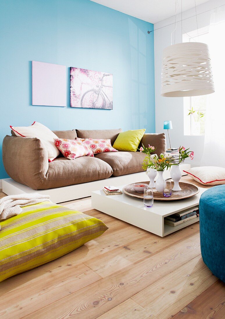 Colourful scatter cushions on sofa and floor and low coffee table with vases of flowers on tray