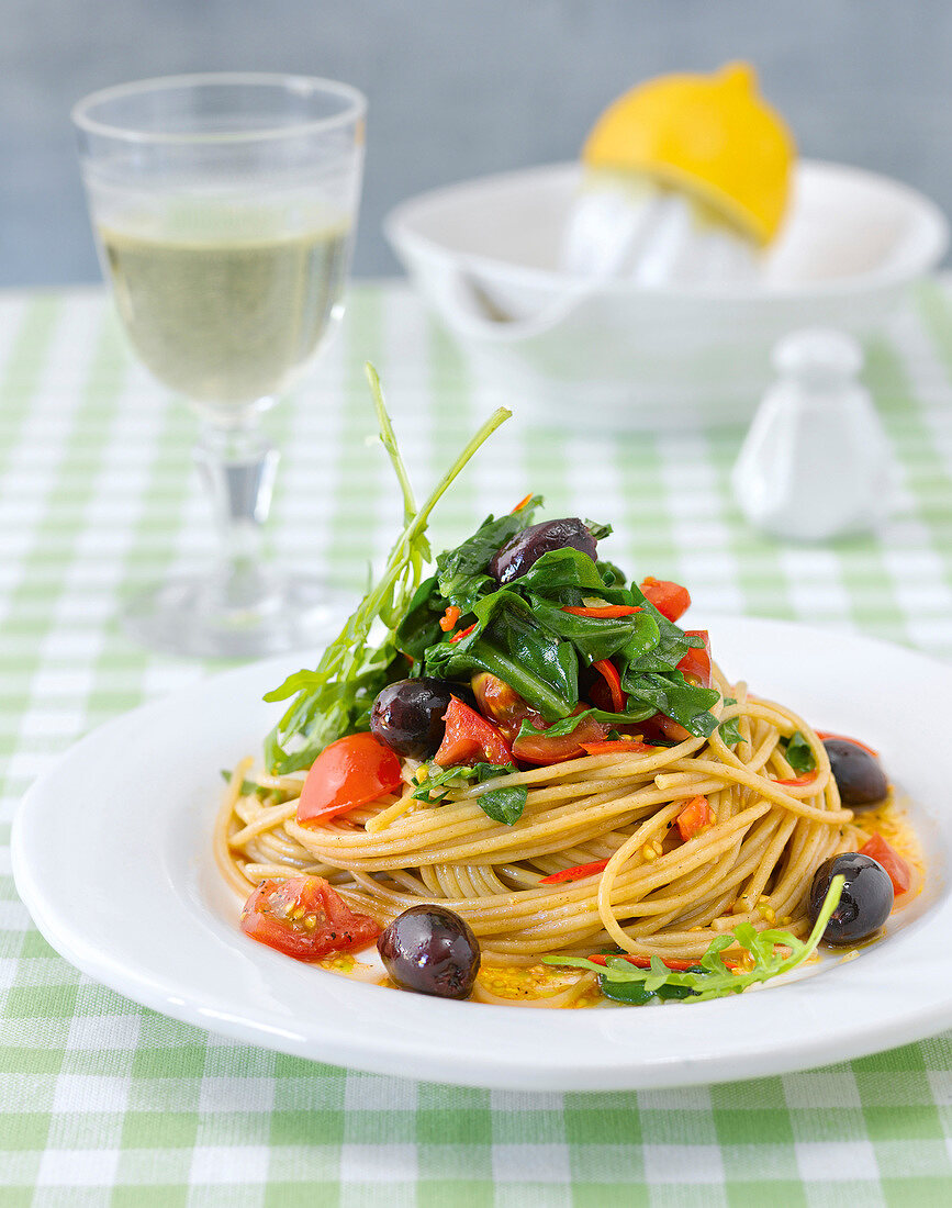 Spaghetti with rocket leaves and black olives on plate, express cooking