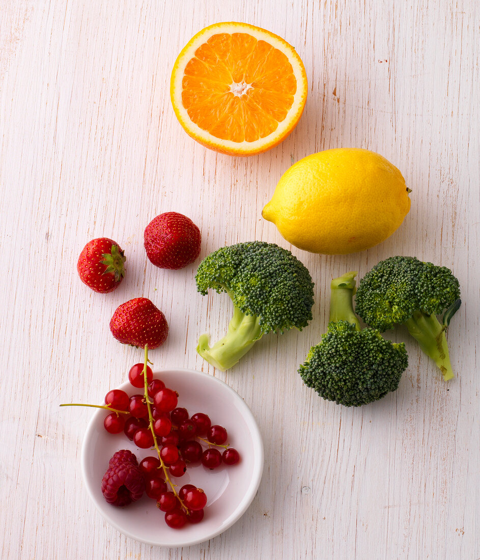 Lemon, oranges, broccoli and berries on wooden surface - food rich in vitamin C