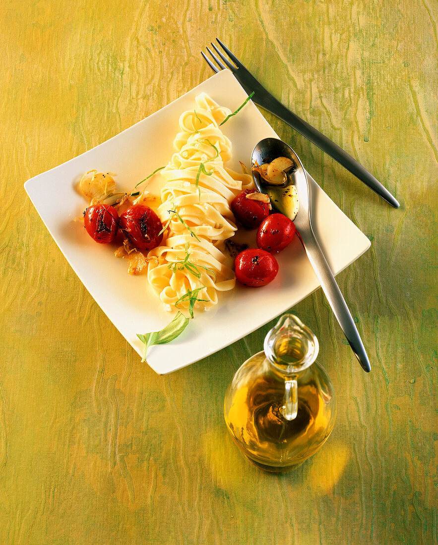 Pasta with tomatoes and garlic on plate and olive oil in carafe