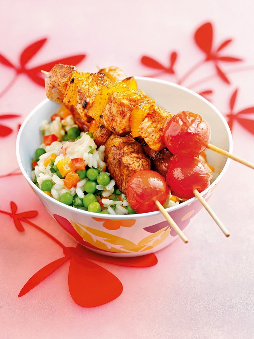 Pork skewers with peppers and tomatoes on a bed of vegetable rice