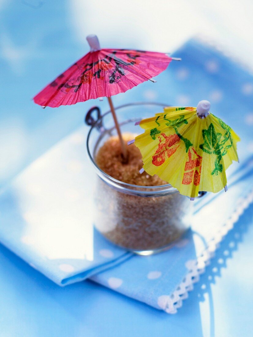 A glass of cane sugar decorated with two colourful cocktail umbrellas