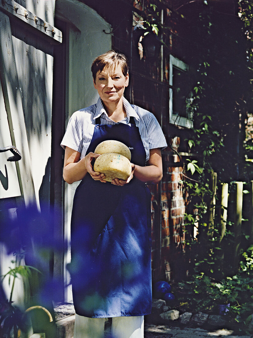 Portrait of mid adult woman holding two loaves of Caprino cheese